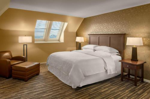 - une chambre avec un grand lit blanc et une chaise dans l'établissement Sheraton Suites Akron Cuyahoga Falls, à Cuyahoga Falls