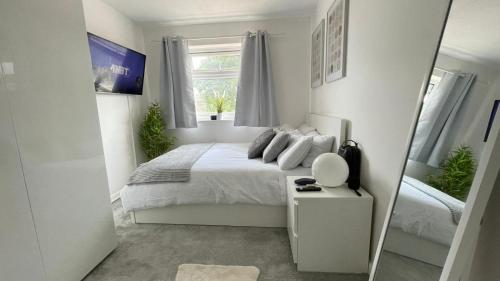 a white bedroom with a bed and a mirror at Lovely 3 bedroom house near city centre - Basildon in Basildon