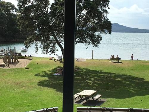 a park with picnic tables and a tree and the water at Beachside Bliss Castor Bay - Holiday by the Beach in Auckland