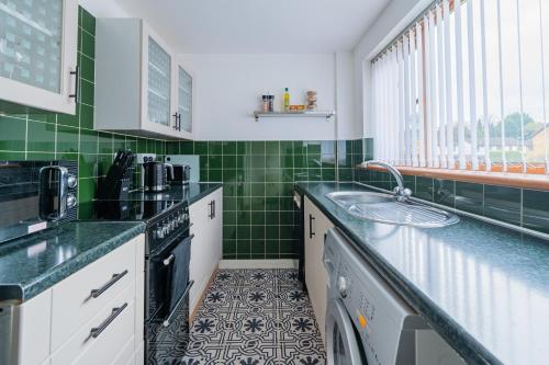 eine Küche mit grünen Fliesen und einem Waschbecken in der Unterkunft A Cosy Home from Home in Middleton
