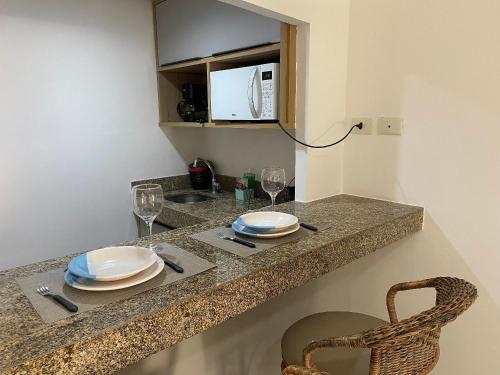 a kitchen counter with plates and glasses and a microwave at Bela Hospedagem - Marinas Flat - Excelente localização na orla de Cabo Branco in João Pessoa