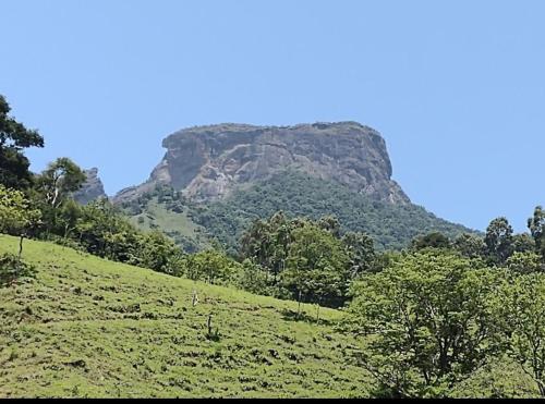 a green hill with a mountain in the background at Tapovan in São Bento do Sapucaí