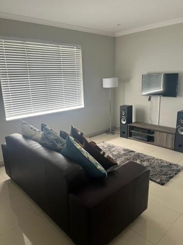 ein Wohnzimmer mit einem schwarzen Sofa und einem TV in der Unterkunft 10 Glen Court in Durban