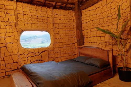 um quarto com uma cama numa parede de tijolos com uma janela em Mơ Niê Farmstay & Cafe em Kon Von Kla
