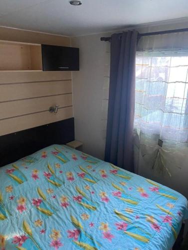 - une chambre avec un lit doté d'un couvre-lit floral et d'une fenêtre dans l'établissement Mobil-home au Camping familial 4 étoiles Les Sables d'Or, au Cap d'Agde