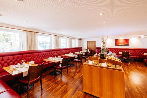 un restaurante con cabinas rojas, mesas y sillas en Sonne 1806 - Hotel am Campus Dornbirn en Dornbirn