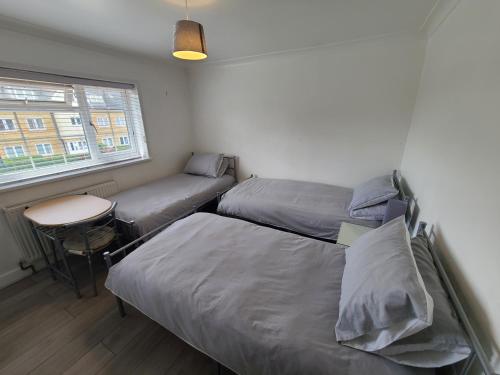 a bedroom with two beds and a table and a window at GATWICK ROOMs-TRAVEL SERVICE-AIRPORT PARKING in Ifield
