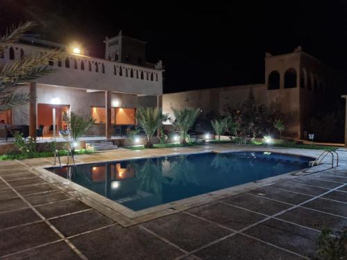 a swimming pool in front of a house at night at Auberge Famille Benmoro in Skoura