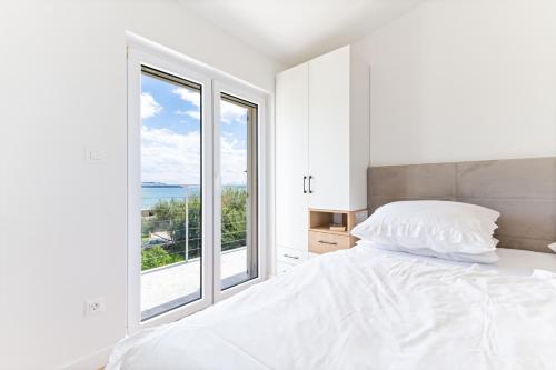 een witte slaapkamer met een bed en een groot raam bij Apartments Stari Resnik in Kaštela