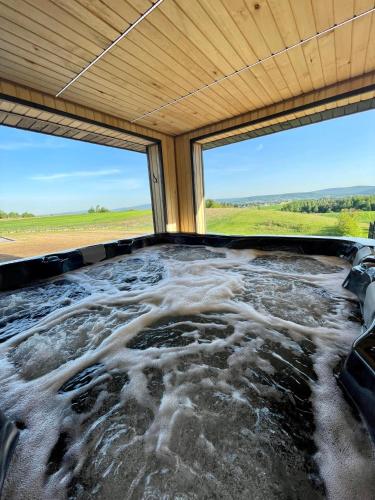 a bathtub with water in a room with a window at Stodoła Na Kresach - widokowy domek drewniany, całoroczny JACUZZI & SAUNA in Bodzentyn