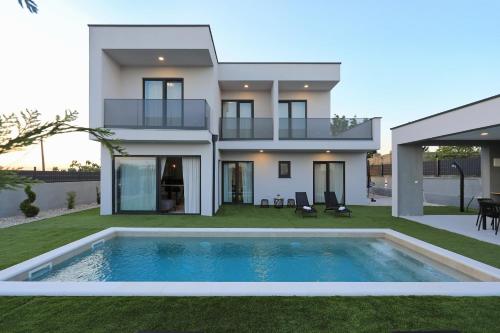 a villa with a swimming pool in front of a house at Villa Cvit Mediterana with heated pool in Knežević