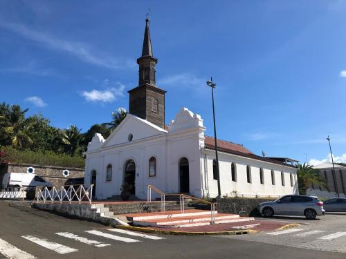 a small white church with a steeple on a street at Face à la Plage avec Parking Sécurisé Appartement de Luxe ou Suite Privée avec Coin Petit Déj selon Disponibilité in Le Diamant