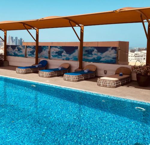 una piscina con dosel y sillas junto a ella en The Avenue Hotel, en Doha