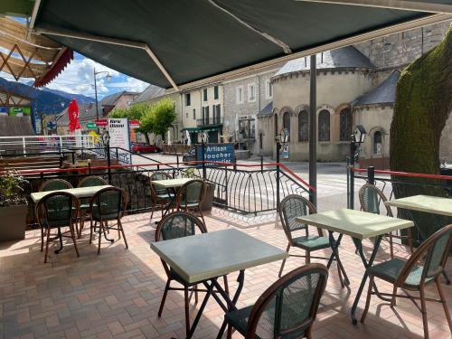 un patio al aire libre con mesas y sillas y un edificio en Hôtel Elaïa, en Corps