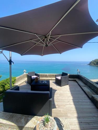 a patio with an umbrella and chairs and the ocean at Maison en bord de mer en Corse Lavasina Brando in Brando