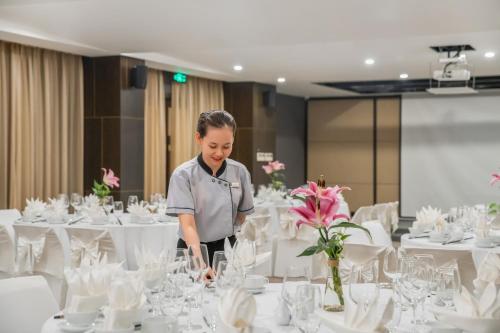 a woman standing in front of a table with white tables at Satya Da Nang Hotel Han Market in Da Nang