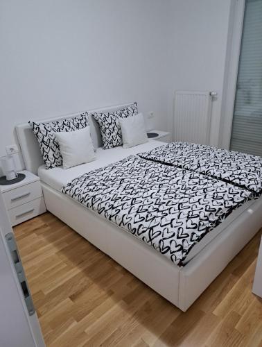 a white bedroom with a bed with black and white sheets at Apartman San in Posušje