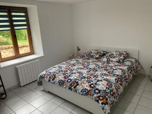 a bedroom with a bed with a floral comforter and a window at Maison proche lac de Madine in Buxières-sous-les-Côtes
