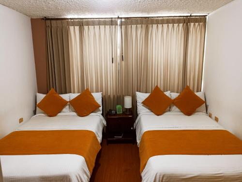 two beds in a hotel room with orange pillows at Hotel Tuvalu in Paipa