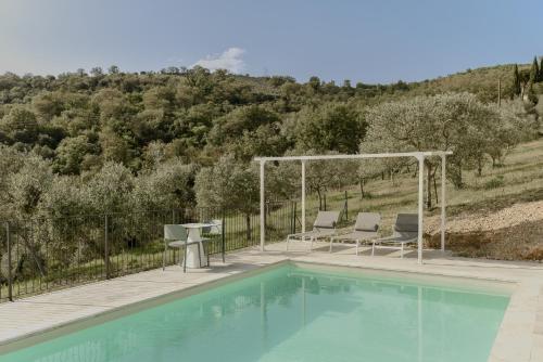 a swimming pool with two chairs and a table next to a hill at Agriturismo Il Mulino delle canutole in Magione