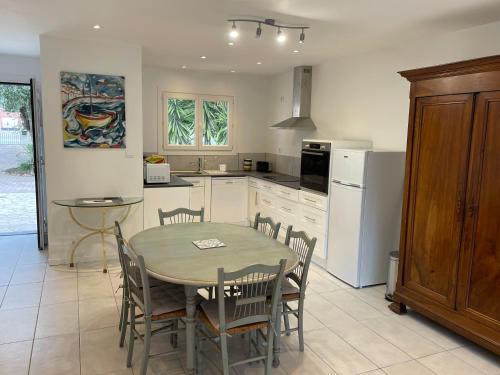 une cuisine avec une table, des chaises et un réfrigérateur dans l'établissement Maison plain pied au calme sur parcelle arborée, à Argelès-sur-Mer