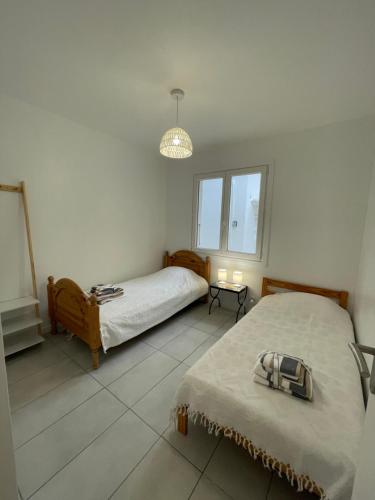 Habitación blanca con 2 camas y lámpara en Maison plain pied au calme sur parcelle arborée, en Argelès-sur-Mer