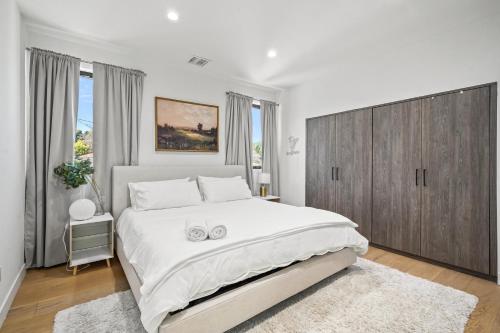 a white bedroom with a large bed with a wooden cabinet at Scandinavian 2BR, 2Bath Townhome, Pet & Kid Friendly, Free Parking, 10min to Venice Beach! in Los Angeles