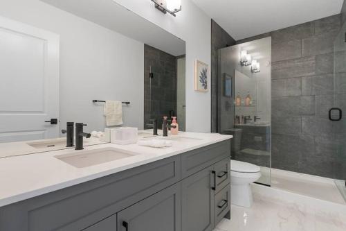 a white bathroom with two sinks and a toilet at Family Home Retreat - 9 mins to WEM - Vintage Arcade-Ping Pong -Air Conditioning in Edmonton