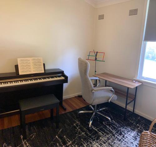 a piano and a chair in a room at Cottage with Piano, Books & Games in the Hunter in Singleton