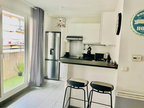 une cuisine avec deux tabourets et un réfrigérateur en acier inoxydable dans l'établissement Appartement 4 pers à 5 min de Paris, à Saint-Ouen