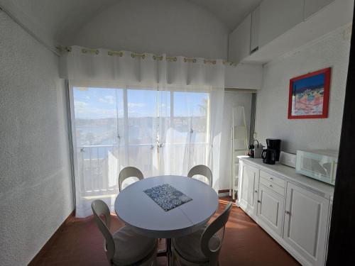 une table et des chaises dans une pièce avec une grande fenêtre dans l'établissement Le Bellevue YourHostHelper, à Gruissan
