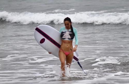 Una mujer caminando hacia el océano con una tabla de surf en Hermanos Perdidos Surf, en Las Tunas