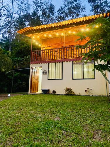 a house with a deck and a lawn in front of it at Cabaña Monarca in Turrialba