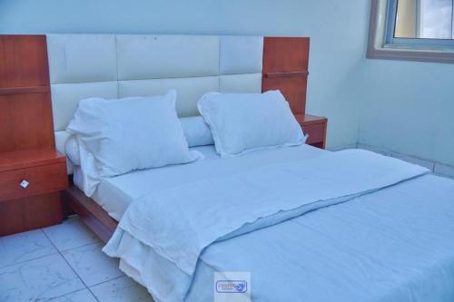 un letto con lenzuola e cuscini bianchi in una stanza di Akouma immo a Emana