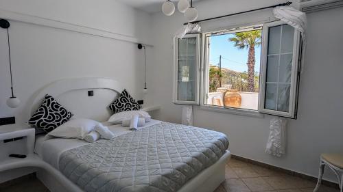 a white bedroom with a bed and a window at Anoi House by the sea Agios Fokas Tinos in Tinos Town