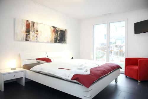 a white bedroom with a bed and a red chair at Reloc Serviced Apart. Wallisellen in Wallisellen