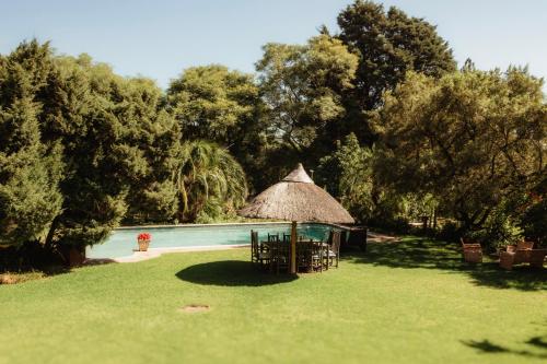 a table and chairs and a straw umbrella next to a pool at Blue Hills Lodge in Midrand