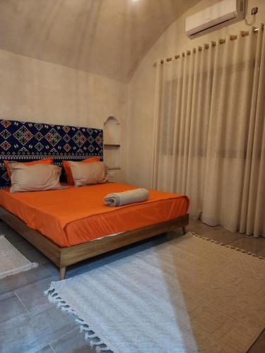 a bedroom with a bed with orange sheets and a window at دار عزيزي in El Guecheïne