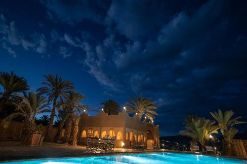 a building with palm trees and a swimming pool at night at Lodge Hara Oasis in Agdz