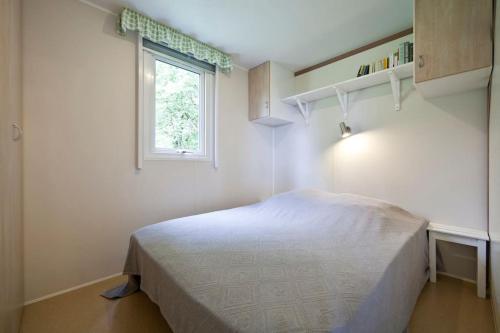 une chambre blanche avec un lit et une fenêtre dans l'établissement Chalet les chênes verts - Périgord proche grottes de Lascaux, à Saint-Amand-de-Coly