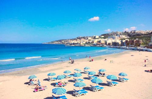 uma praia com guarda-sóis azuis e brancos e o oceano em 3 Balconies South Views Special Bedroom 5 mins to beach em Mellieħa