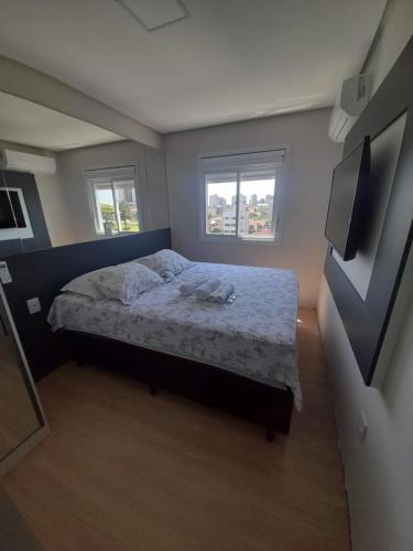 a small bedroom with a bed and two windows at Apartamento bem localizado in Bento Gonçalves