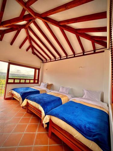three beds in a room with a large window at Hospedaje la Villa de Juan in Villa de Leyva
