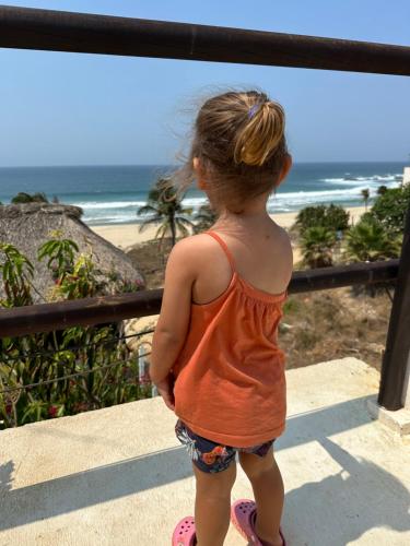 a little girl standing on a balcony looking at the beach at Beachfront Paradise Boutique Hotel in Santa María Tonameca