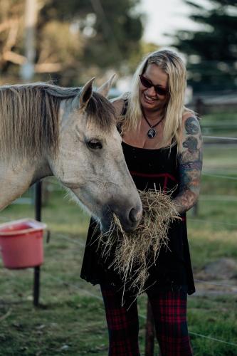 a woman holding a pile of hay next to a horse at Galahad's Animal Sanctuary B&B in Gisborne