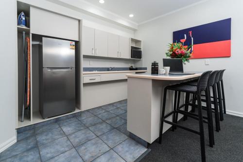 a kitchen with a refrigerator and two bar stools at Aubyn Court Spa Motel in Palmerston North