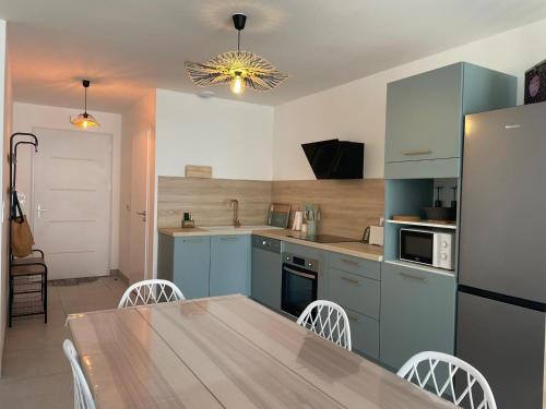 une cuisine avec des placards bleus et une table avec des chaises dans l'établissement Charmante maison neuve 3 chambres, WIFI, proche forêt domaniale, avec jardin et parking privé - FR-1-323-538, à Saint-Jean-de-Monts