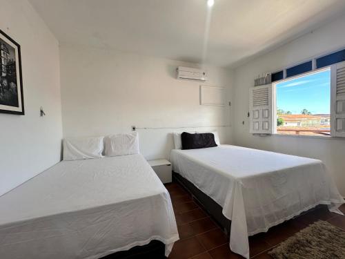 zwei Betten in einem weißen Zimmer mit Fenster in der Unterkunft Casa Pekó Barra de São Miguel (5 suítes) in Barra de São Miguel
