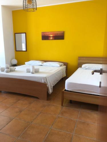 2 Betten in einem Zimmer mit gelber Wand in der Unterkunft Oasi in Porto Cesareo