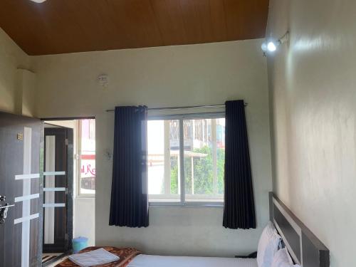 a bedroom with a window with blue curtains at Gugal Residency Mahabaleshwar in Mahabaleshwar